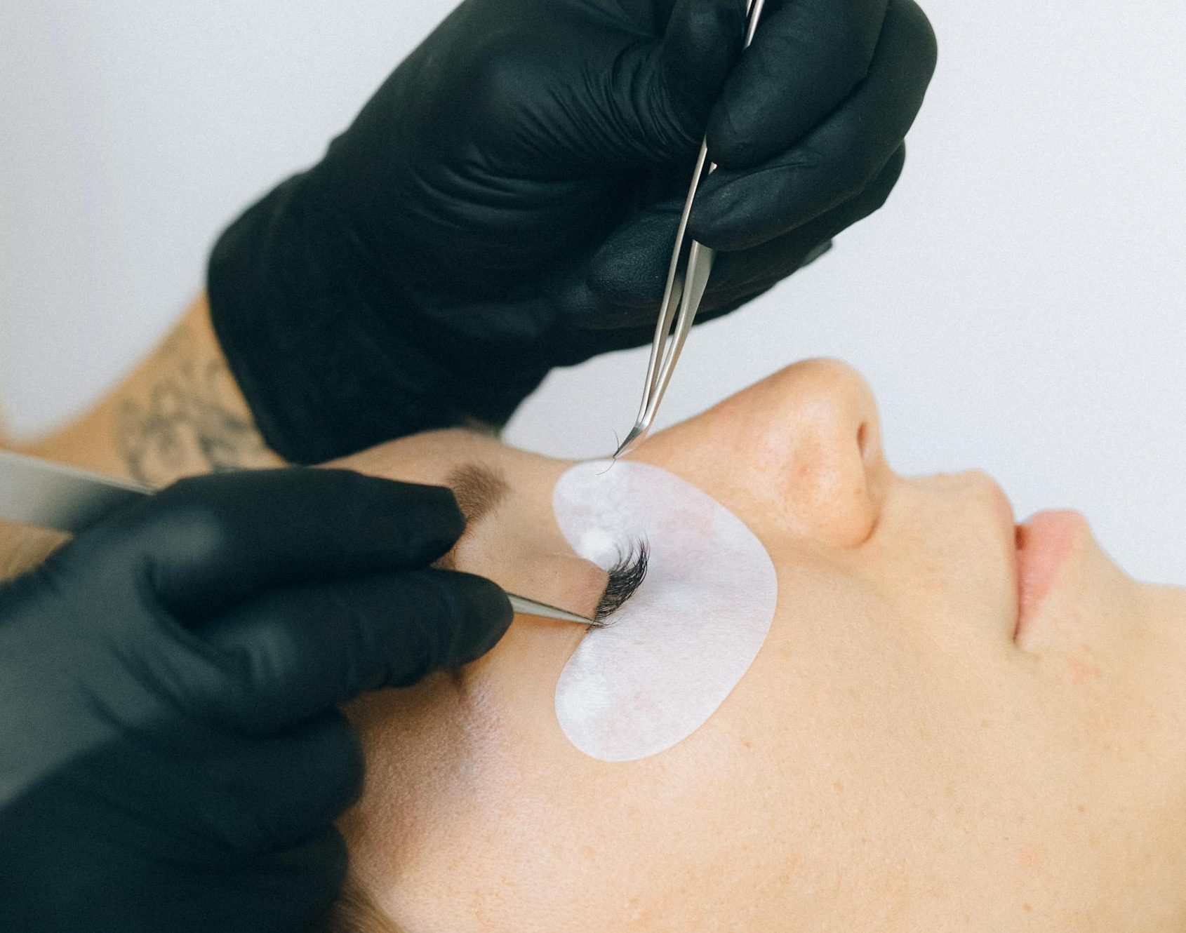 Close-up of a beautician applying eyelash extensions to a client in a salon setting.